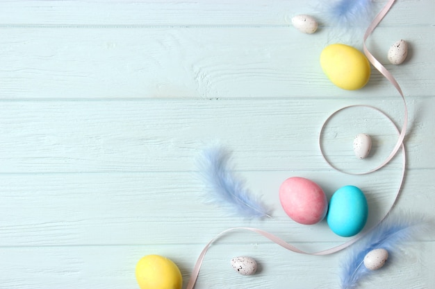 Easter composition of painted eggs and feathers on a colored background