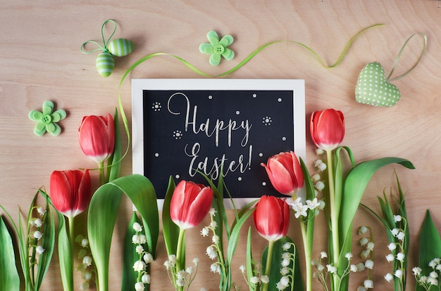 Easter composition with blackboard framed with spring flowers, tulips and lily of the valley, text