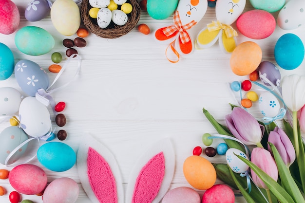 Easter composition with colored eggs, rabbit ears, candy, nest and tulips 