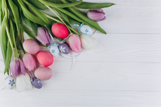 Easter composition with colored eggs and tulips on a white wooden background.