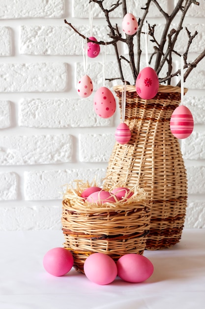 Easter composition with decorated tree branches in a wicker vase and pink colored eggs in wicker basket on white background. Copy space