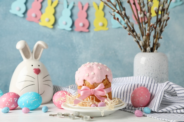 Easter composition with Easter cake and eggs on white wooden table against blue surface