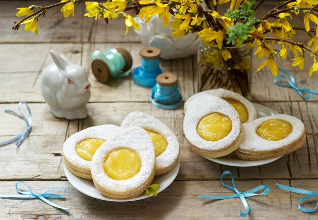 Easter composition with egg-shaped cookies filled with lemon curd, rabbit, bouquet of forsythia and bows.