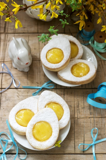 Easter composition with egg-shaped cookies filled with lemon curd, rabbit, bouquet of forsythia and bows.