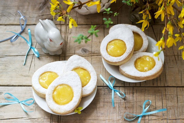 Easter composition with egg-shaped cookies filled with lemon curd, rabbit, bouquet of forsythia and bows.