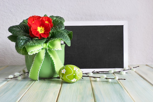 Easter composition with painted Easter eggs and red primrose pot flower on rustic wood