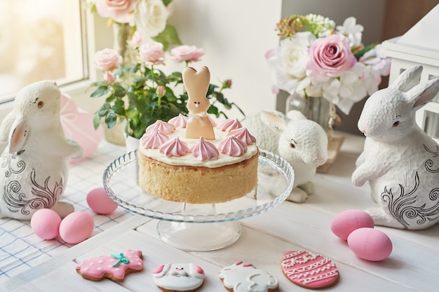 Easter composition with sweet cake with strawberry icing, ceramic bunnies, pink eggs and roses