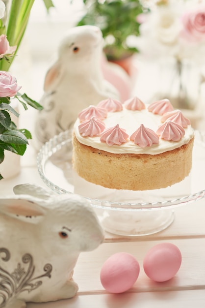 Easter composition with sweet cake with strawberry icing, roses and ceramic bunnies