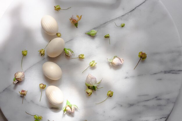 Фото Пасхальная композиция с яйцами из белого шоколада, весенними листьями и цветами на мраморе пастельных тонов