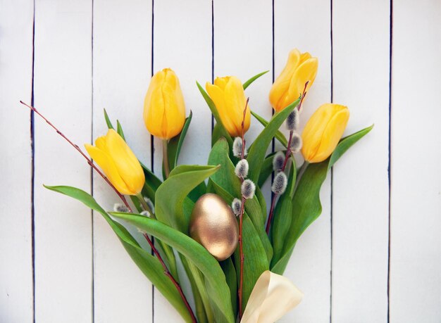 Easter concept Bouquet of yellow tulips willow branches with a golden egg