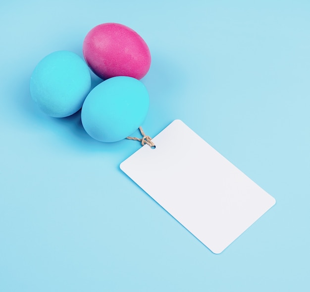 Easter concept. Colored eggs with blank tags isolated on blue background with copy space