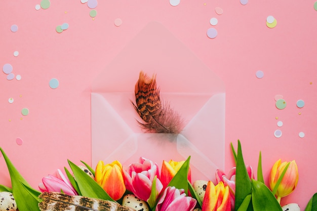 Easter concept, confettia nd open matte envelope with feathers, tulips and quail eggs on pink background