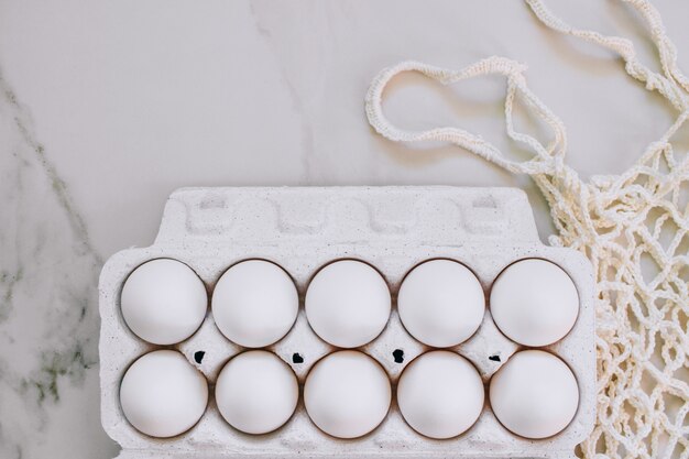 Foto concetto di pasqua, uova di pollo piatto e borsa eco su fondo di marmo. vista dall'alto.