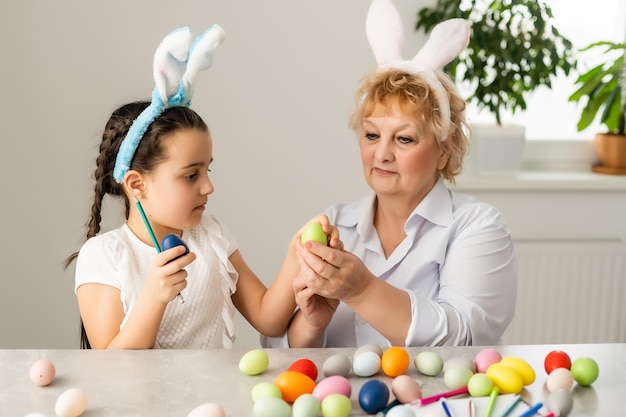 Easter concept. Grandmother with granddaughter are holding Easter eggs at home.