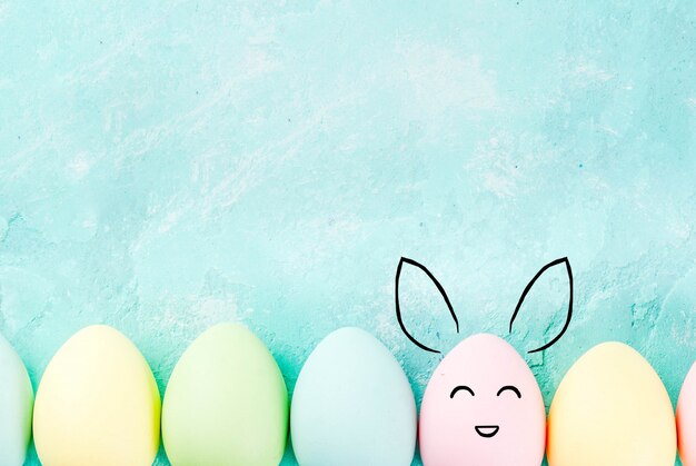 Easter concept, pastel colored eggs on a light blue background, with painted rabbit muzzles and ears. Background for greeting card, copy space