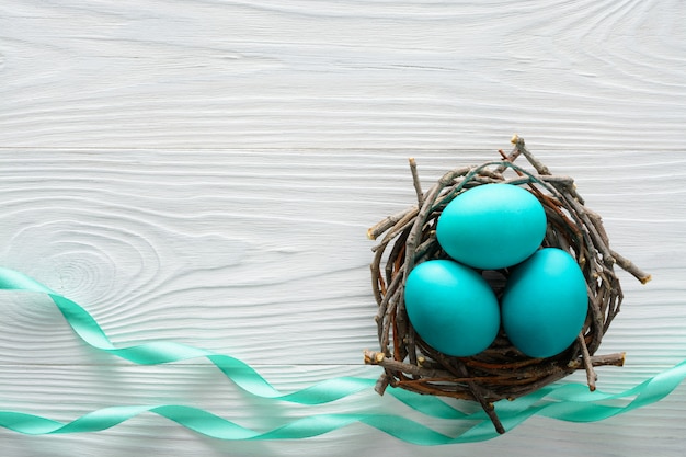 Easter concept with blue eggs in the nest on wooden table.