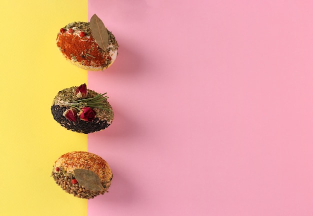 Easter concept with eggs decorated with different spices and cereals without dyes and preservatives on pink and yellow background, Space for text