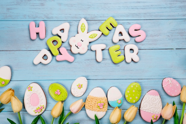 Easter cookies letter Happy Easter and colorful eggs with tulips on wood background
