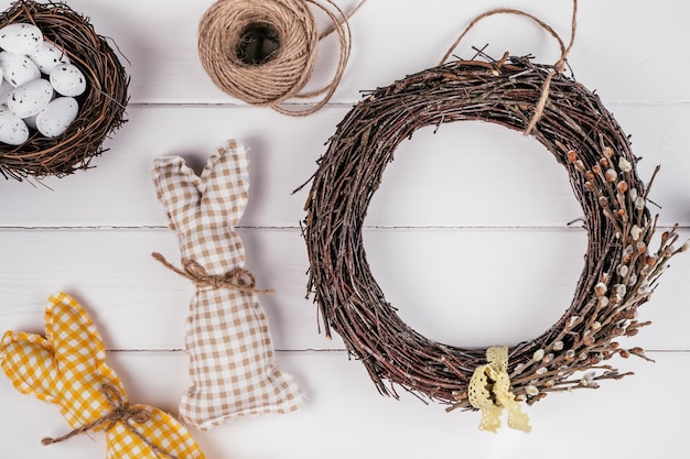 Easter crafting woven willow wreath with tape bow White planking wall background Eggs nest and toy rabbits invitation Tradition festive seasonal decoration step by step Workshop ornament Top view