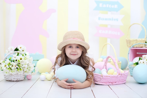 Easter! Cute girl playing with easter egg. A child holds a large colorful egg on the background of Easter interior. Easter colorful decor in the home, a basket of colorful eggs. Spring room interior