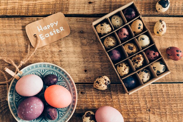 Easter decor. Top view of colored Easter eggs on plate and Easter quail eggs in box lying on wooden rustic table