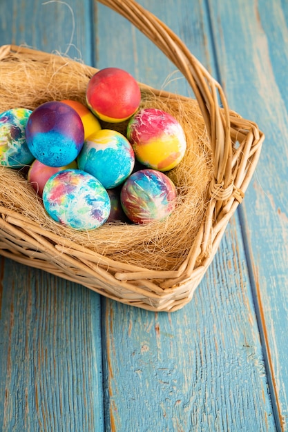 Easter decorated eggs in a basket on the hay on turquoise wooden background.