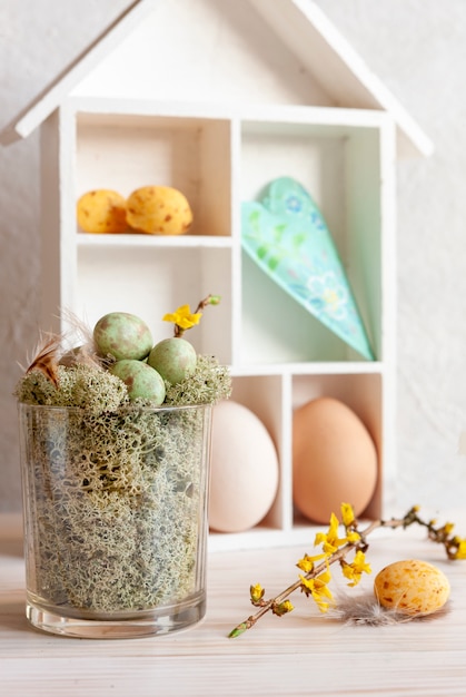 Foto decorazioni pasquali uova di pasqua nel nido, uova di quaglia, fiori primaverili e piume nel vaso di vetro