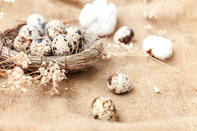 茶色の素朴なリネンのキャンバステーブルに巣と綿の卵とイースターの装飾