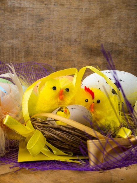 Фото Пасхальная декоративная композиция с желтыми цыплятами, цветными яйцами и разноцветными перьями на деревянной доске