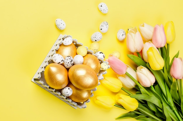 Easter dekorations. decorative golden eggs, pussy-willow twigs  and tulips on yellow background