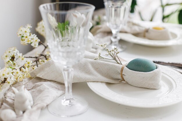 Easter egg in bunny napkin on plate with cutlery bunny spring\
flowers on rustic white table