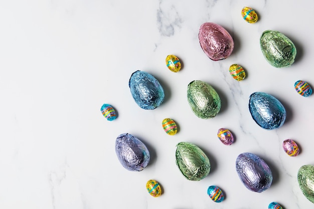 Le prelibatezze al cioccolato all'uovo di pasqua si avvolgono in un foglio colorato lucido su uno sfondo di marmo