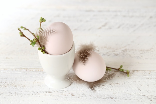 Easter egg close-up with feather and twig with buds on a white shabby chic table on a light blurred