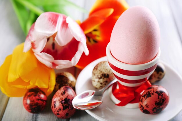 Easter egg in holder and tulip flowers on wooden background