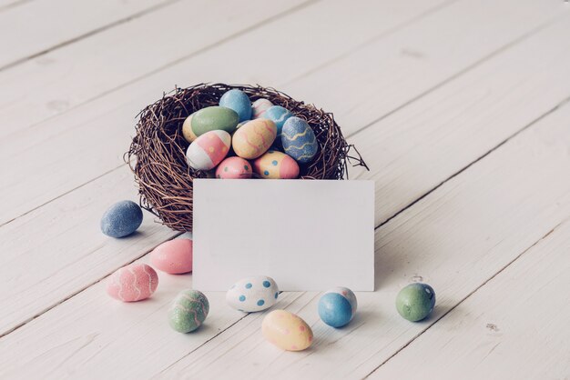 Easter egg and nest with blank paper on wood table background, copy space.