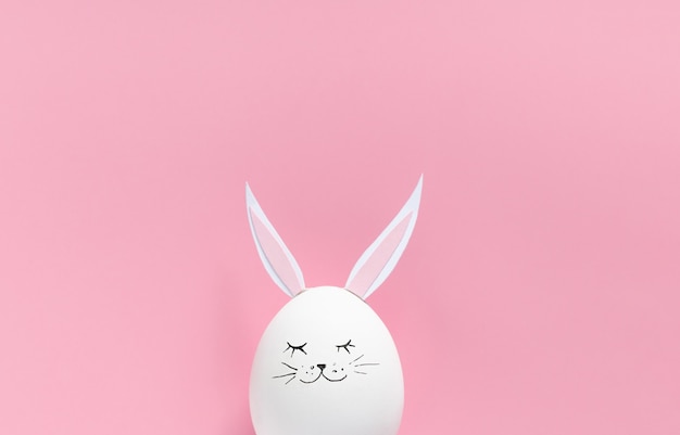 Easter egg with bunny ears and face on pink background with copy space. Flat lay or top view. Minimal concept. Conceptual creative photo approaching Happy Easter holiday.