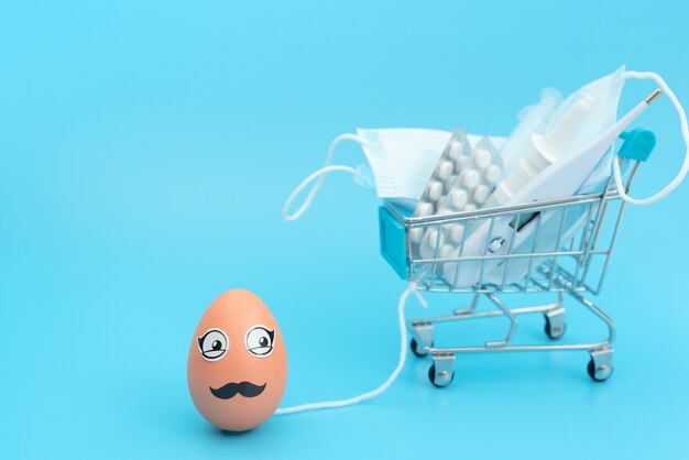 Easter egg with eyes and moustache is carrying blurred shopping trolley with medical face mask