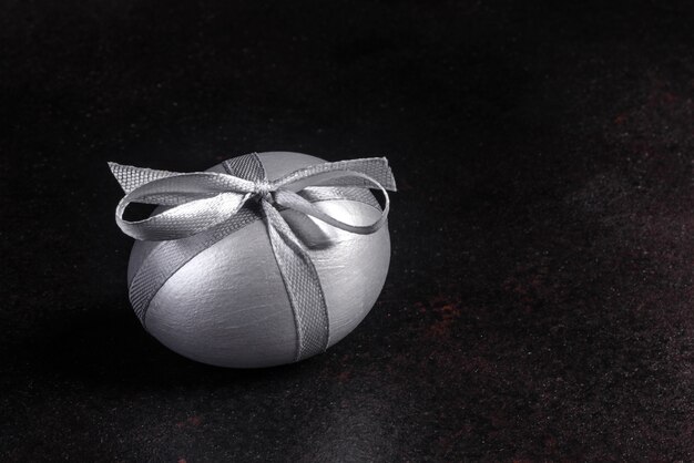 Easter egg with gift tape on a dark wooden table. Preparation for the holiday