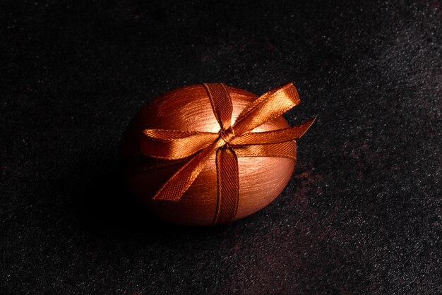 Easter egg with gift tape on a dark wooden table. Preparation for the holiday