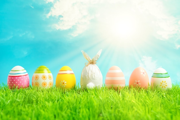 Photo easter egg wrapped in a paper in the shape of a bunny with colorful easter eggs on green grass.