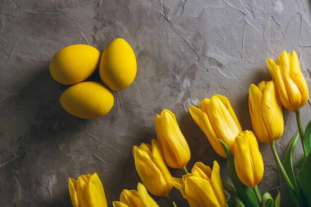 Пасхальные яйца и букет ярко-желтых тюльпанов на серой бетонной поверхности