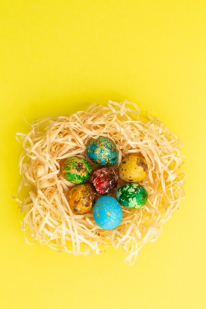 Easter eggs are painted in red, yellow, blue and green. The eggs are in a nest of wood shavings. Painted easter eggs on a yellow background.Flat lay . Copy space