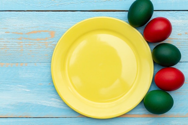 Easter eggs around yellow dish with copy space on a blue wooden .