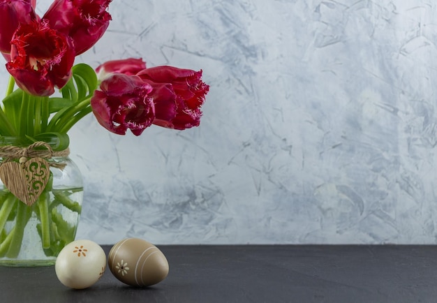 Easter eggs on a background of red tulips in a glass jar