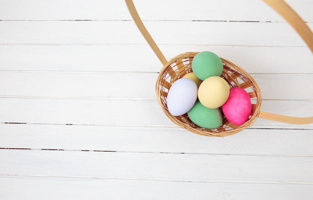 Uova di pasqua in cestino su fondo di legno bianco