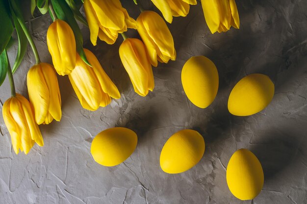 Easter eggs and bouquet of bright yellow tulips on gray concrete surface. Flat lay. Top view