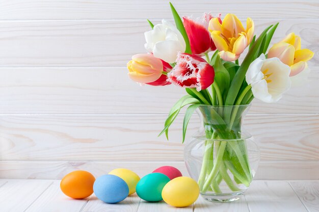 Photo easter eggs and a bouquet of tulips on a wooden table, floral still life. holiday concept.