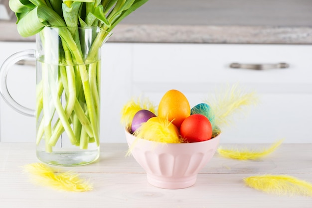 Easter eggs in a bowl with feathers and a bouquet of tulips on the kitchen table