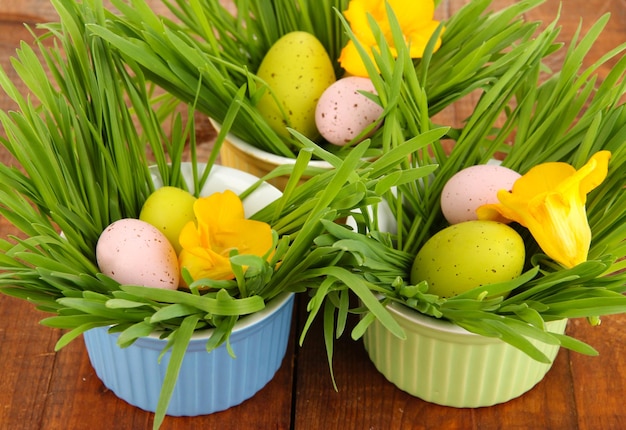 Easter eggs in bowl with grass on wooden table close up