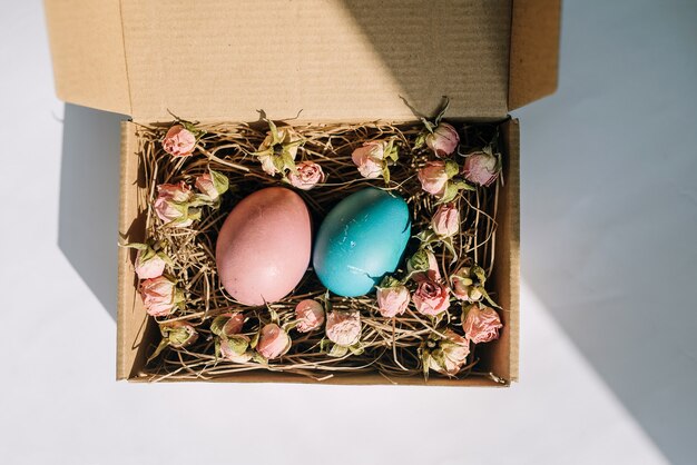 Easter eggs in a cardboard box with flowers on a white background top viewhappy Easter day